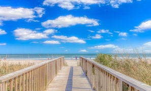 Un paseo marítimo de madera que conduce a una playa, con cielos despejados y vistas al océano.