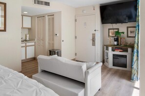 A hotel room with a bed, a sofa, a TV, a fireplace, and a kitchenette.
