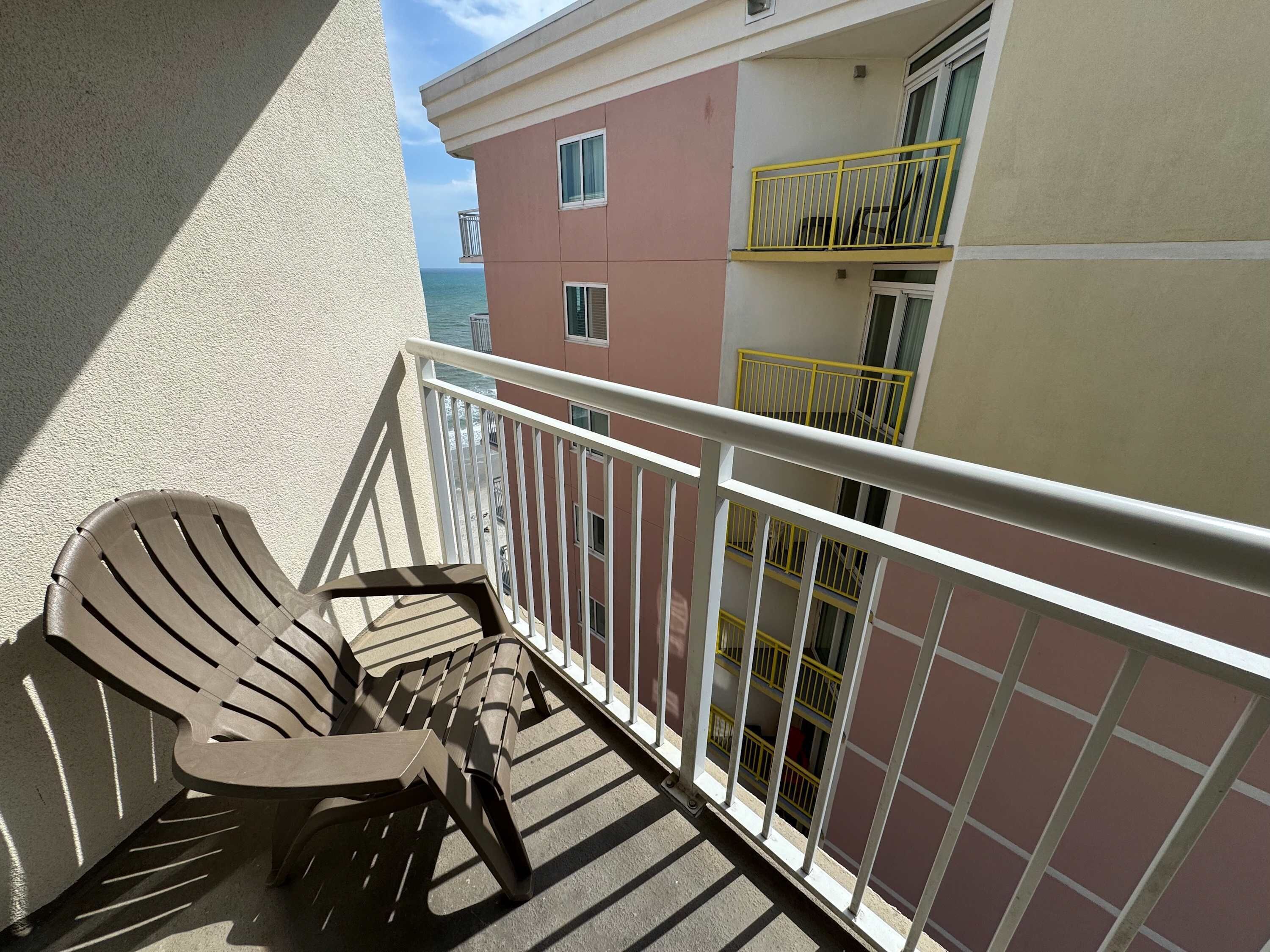 Een balkon met een stoel, een leuning en een gebouw met balkons op de achtergrond.