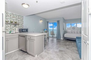 A compact apartment with a kitchenette, a dining area, a balcony with a view, and a bedroom.