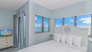 A bedroom with a bed, a TV on a dresser, and a view of the ocean through the windows. - Palace 1505 (Myrtle Beach)