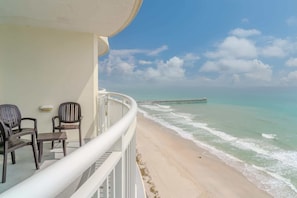 A balcony with chairs overlooking a beach and a pier.