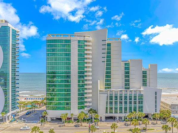A modern hotel with a curved facade, large windows, and a beachfront location.
