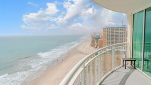 Uma varanda com vista para a praia e o oceano, um corrimão e uma pequena mesa.