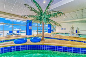 Une piscine intérieure agrémentée d’un palmier, dotée de grandes fenêtres et bordée de carreaux bleus.