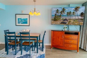 A dining area with a table, chairs, a chandelier, and a painting of a beach scene. - Sandy Beach 1612 (Myrtle Beach)