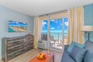 A room with a sofa, a TV, a fruit bowl, and a balcony with a view of the sea.