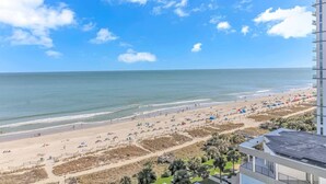 Vista de una playa desde un edificio de gran altura, con cielo despejado, arena y sombrillas.