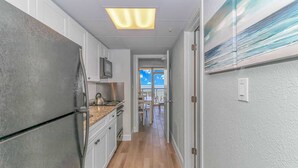 Un pasillo estrecho con una cocina a un lado, un comedor con vistas y una puerta que da a un balcón exterior.