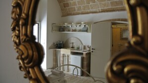 A bedroom with a bed, a dresser, a mirror, and a kitchenette. - Relais la Casa del Poeta (Gallipoli)