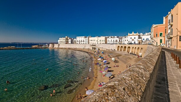 A coastal town with a beach, clear blue waters, and historic buildings along the waterfront. - Relais la Casa del Poeta (Gallipoli)