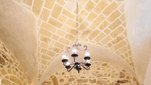 A stone-walled bedroom with a bed, a bench, and a chandelier. - Relais la Casa del Poeta (Gallipoli)