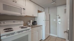 A kitchen with white appliances, a stove, microwave, and refrigerator, and a tiled floor. - Caravelle 422 (Myrtle Beach)