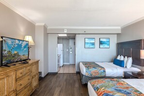 A hotel room with two beds, a TV on a wooden dresser, a door leading to a bathroom, and a view of the ocean.
