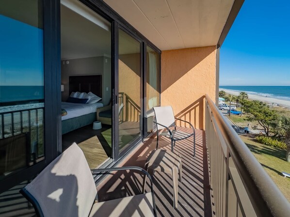 A balcony with a bed, a chair, and a view of the beach.