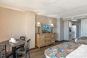 A hotel room with a dining table, two beds, a dresser, and a kitchenette.