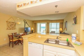 A compact hotel room with a kitchenette, a dining area, a television, and a view of the ocean.
