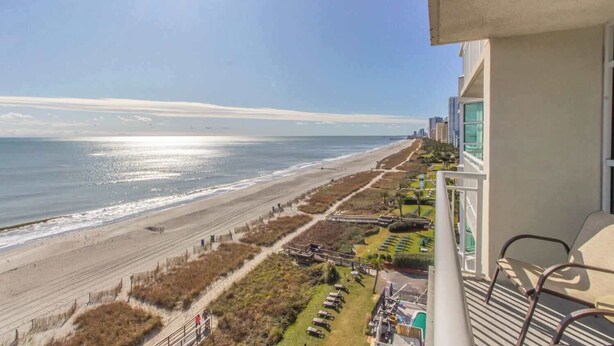 A balcony with a view of a beach and ocean, a pool area, and a building with a balcony. - Carolinian 731 (Myrtle Beach)