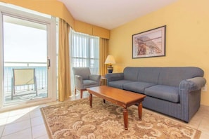 A living room with a sofa, armchair, coffee table, and a view of the ocean through a sliding door.