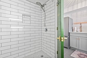 Ein Badezimmer mit weißen Fliesen im U-Bahn-Stil, einer Dusche mit Duschbrause, einer Toilette und einer grünen Tür.