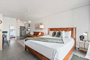 A modern bedroom with a wooden bed, a sofa, a desk, and a kitchenette.