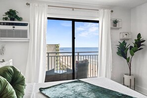 Una stanza con un'ampia porta scorrevole in vetro che si apre su un balcone con vista sulla spiaggia e sull'oceano.