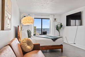 Ein Schlafzimmer mit Bett, einer Couch, einer Pendelleuchte, einem Fernseher und einem Balkon mit Blick.