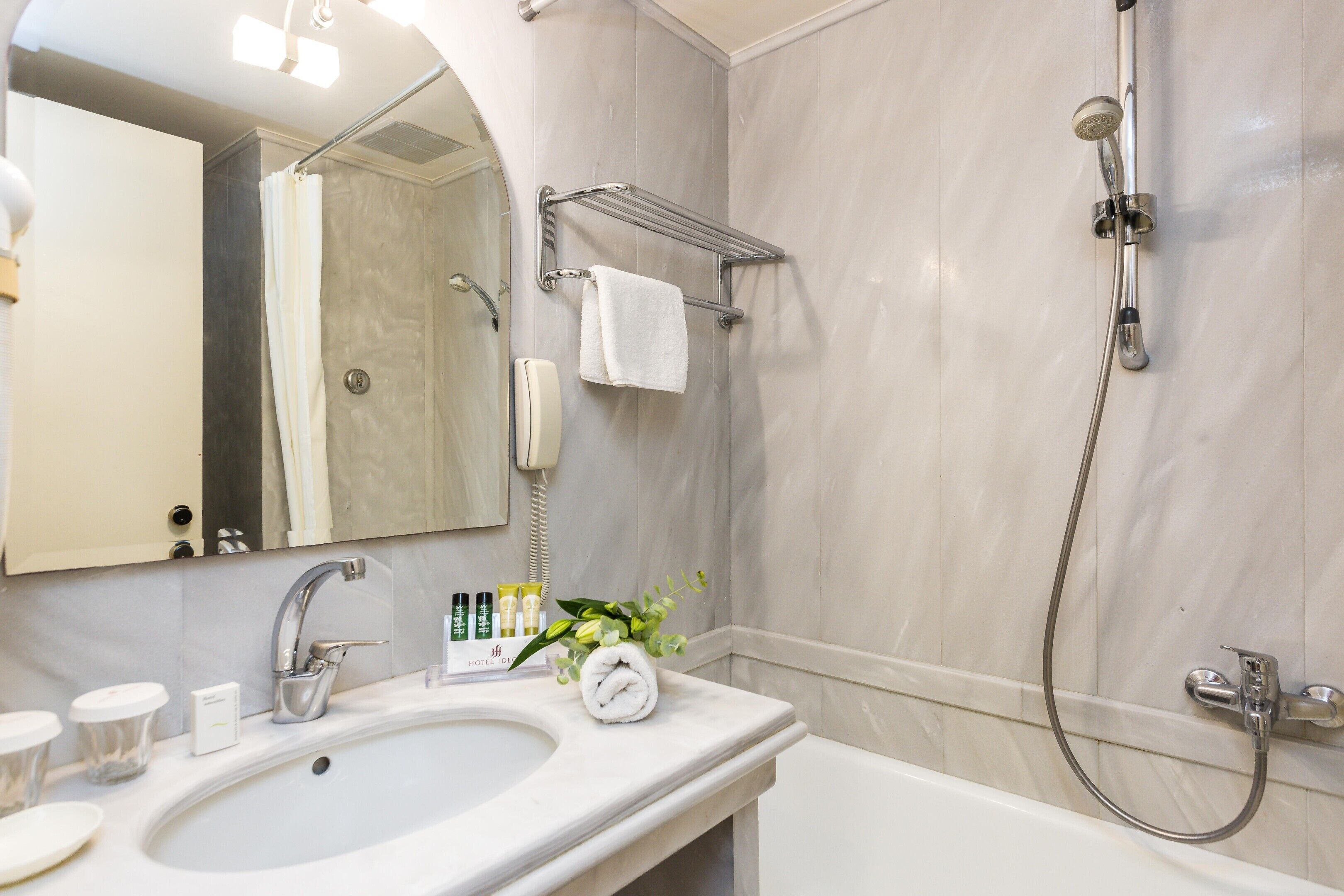 Un baño con lavamanos, espejo, ducha y toallero.