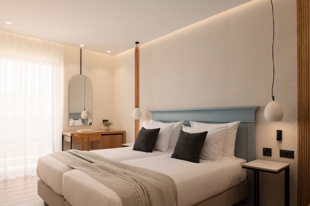 Quarto de hotel moderno com uma cama grande, mesas de cabeceira, uma escrivaninha e um espelho.
