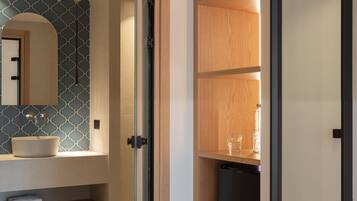 A modern bathroom with a glass door, a sink, a mirror, and a built-in shelf.