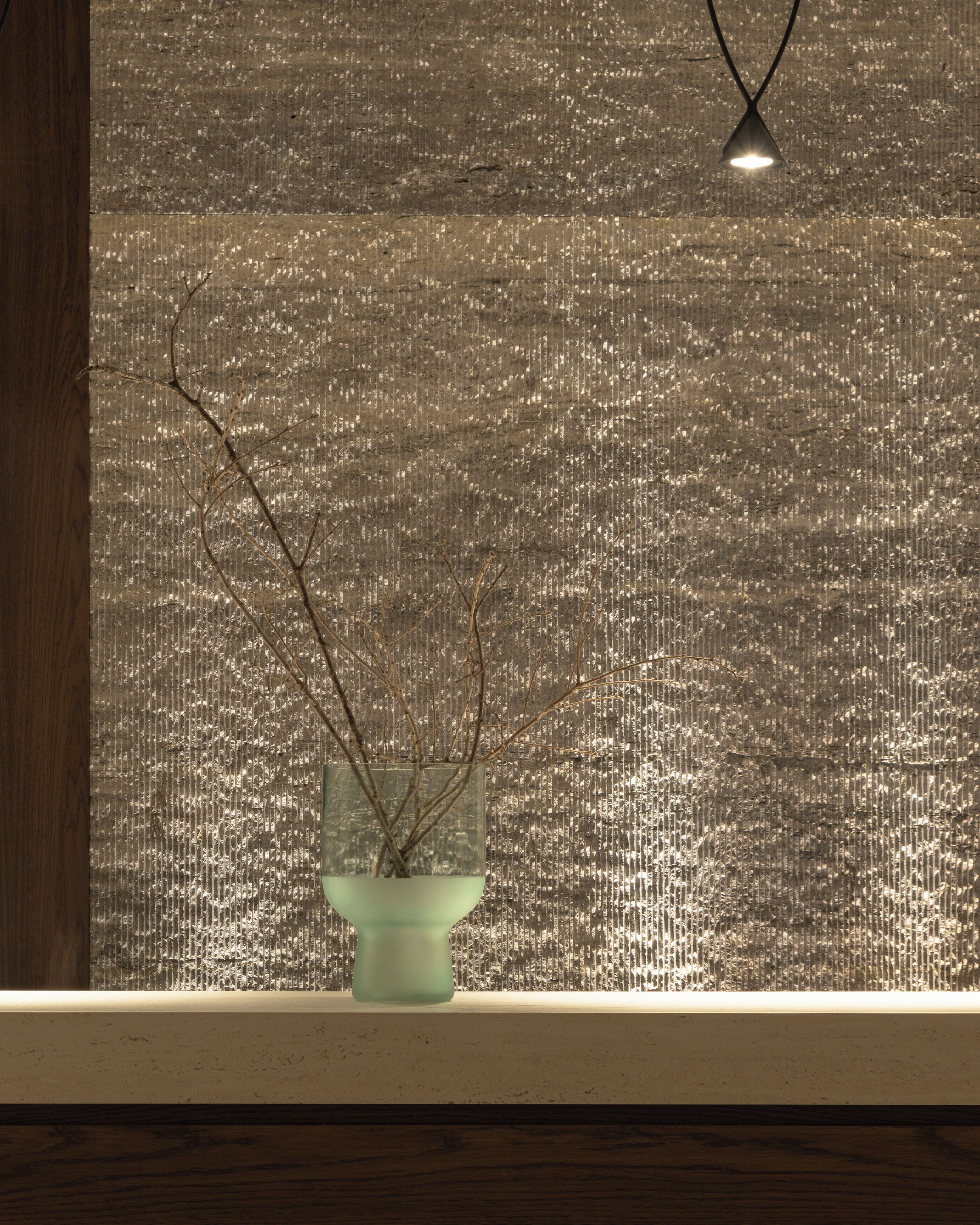 A window with a textured wall and a vase with branches.