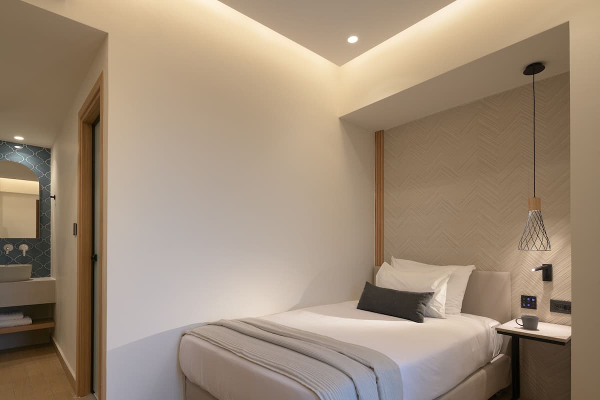 Quarto de hotel moderno com uma cama grande, mesa de cabeceira com luminária, prateleira embutida e espelho.