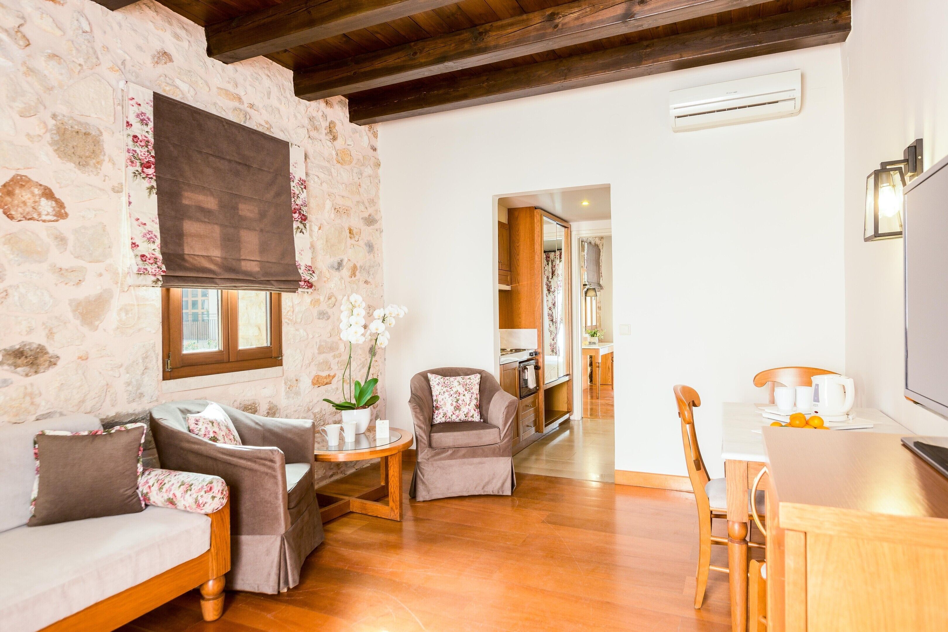A cozy living room with stone walls, a wooden ceiling, a sofa, a coffee table, and a kitchen area in the background.