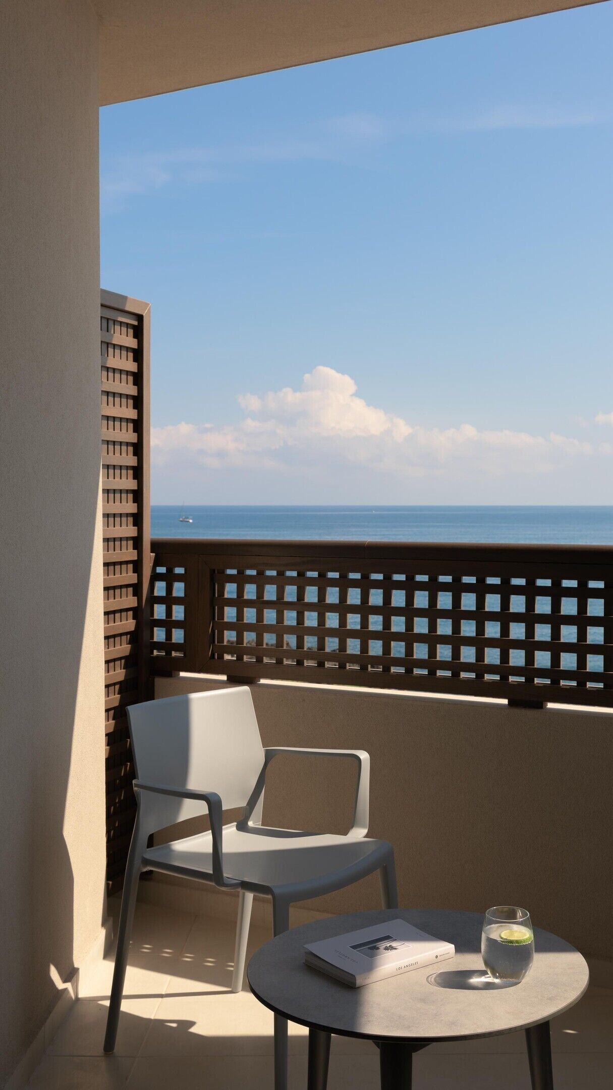 A balcony with a white chair and a small round table, a book, and a glass of water.