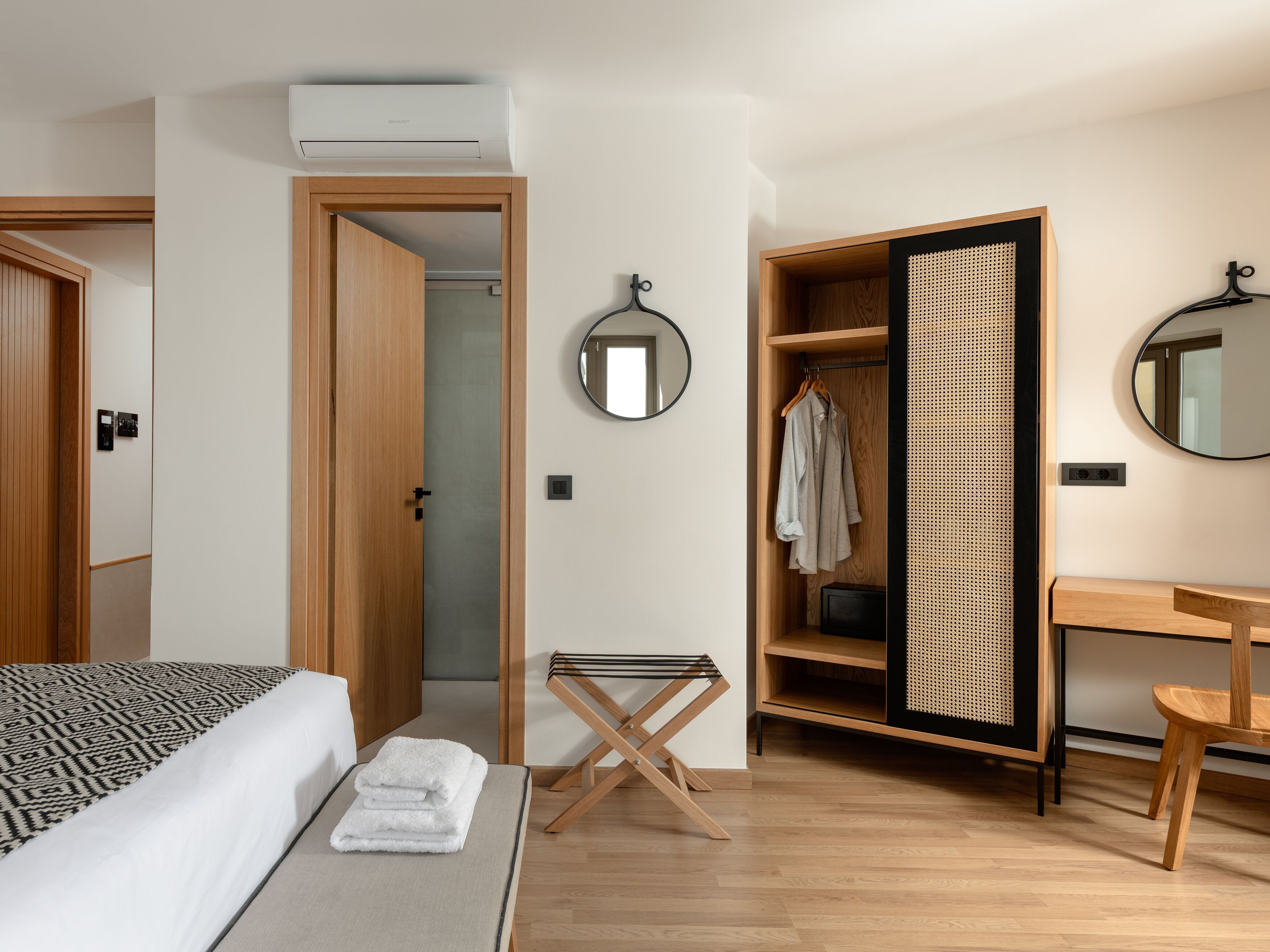 A modern bedroom with a bed, a bedside table, a mirror, a wardrobe, and a small stool.