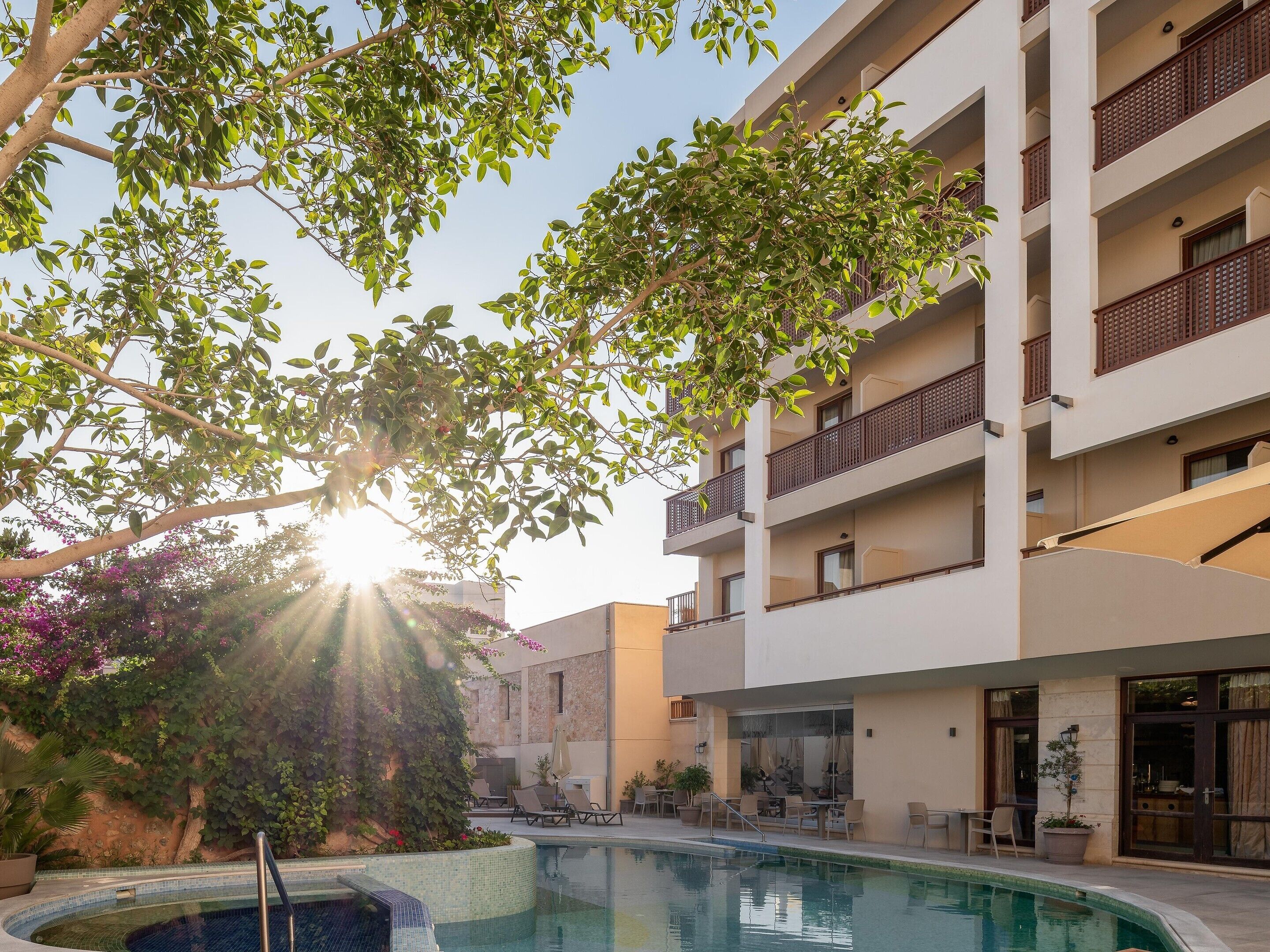 A pool area with a clear view of the sky, surrounded by a building with balconies and outdoor seating.