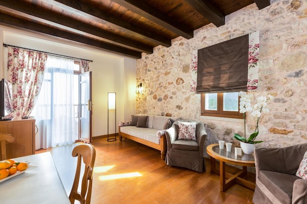 A cozy living room with a stone wall, wooden flooring, and a sofa set. - Hotel Ideon (Rethymno)