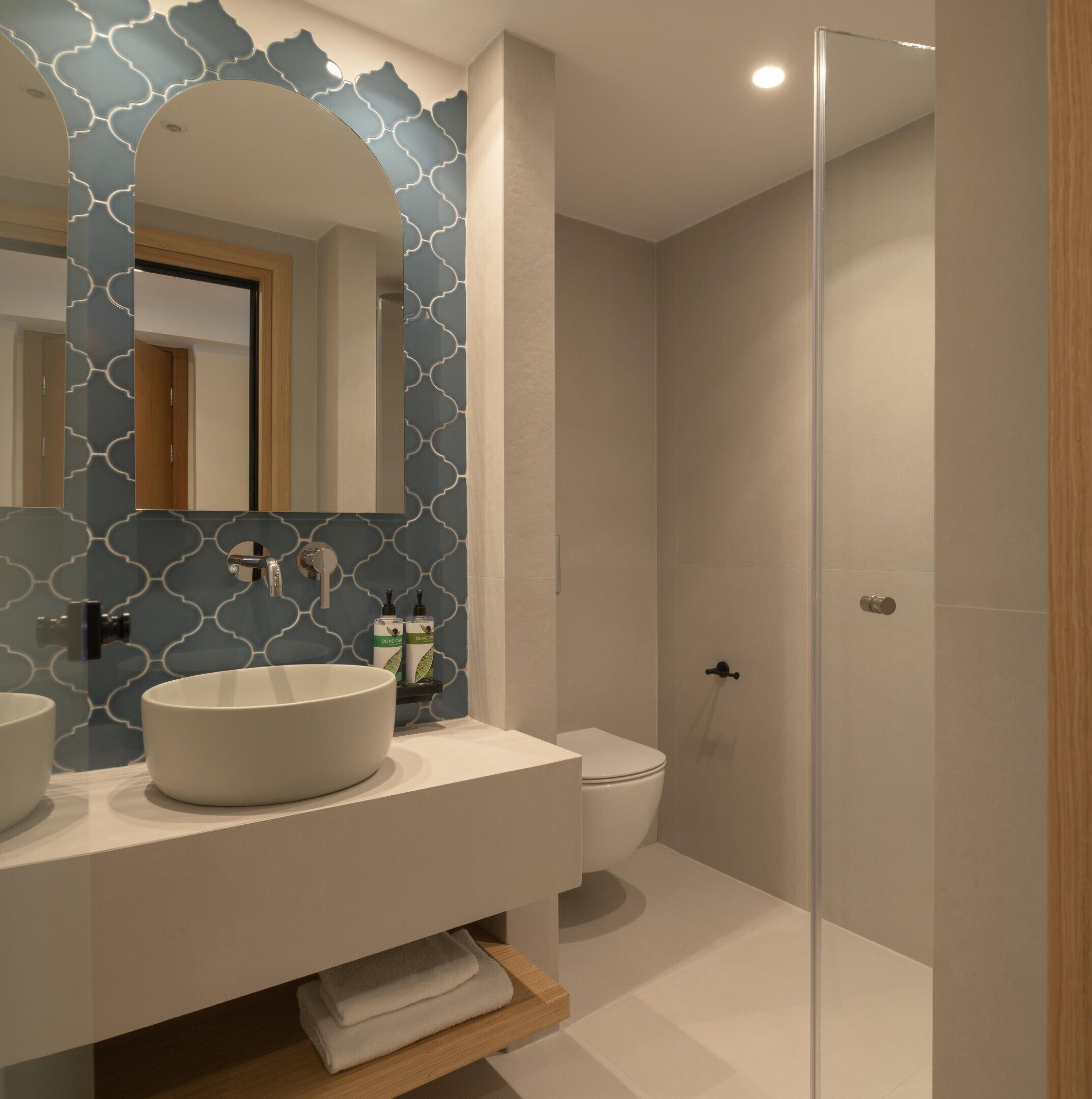 Un baño moderno con un espejo grande, dos lavamanos, un inodoro y una cabina de ducha con paredes de vidrio.