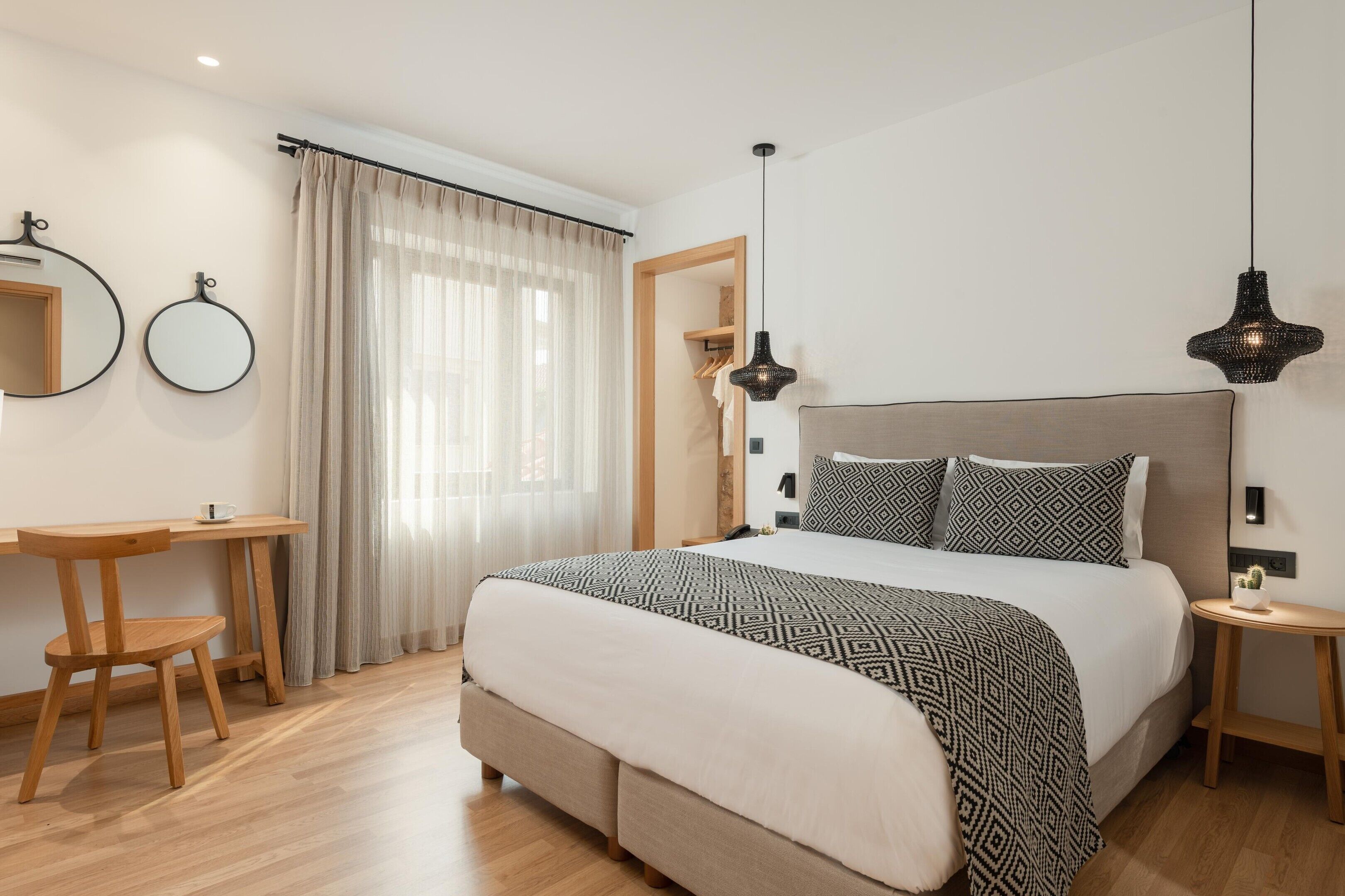 Un dormitorio con cama, mesitas de noche, escritorio, silla y ventana con cortinas.