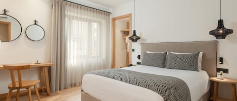 Een slaapkamer met een bed, nachtkastjes, een bureau, een stoel en een raam met gordijnen.