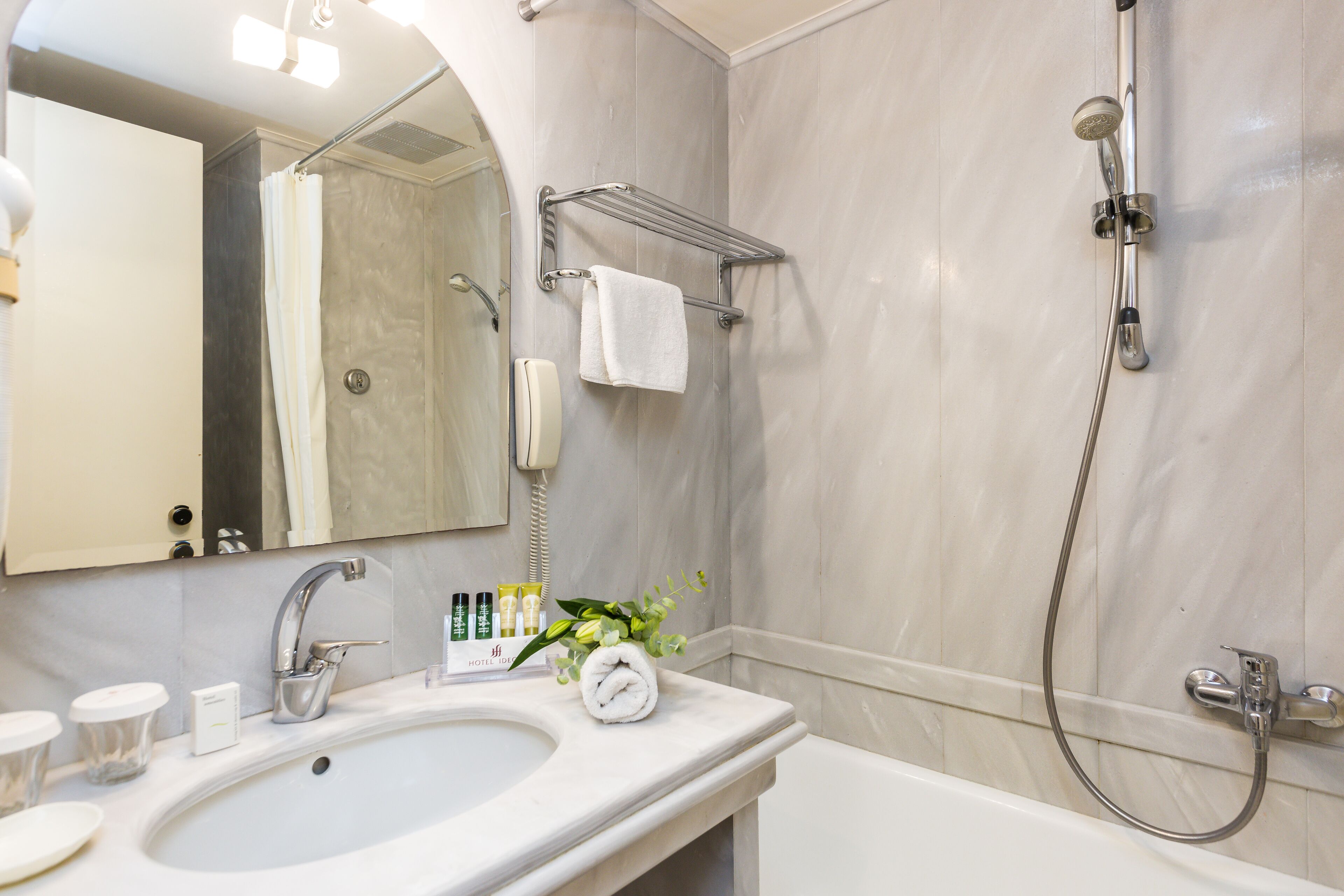Un baño con lavamanos, espejo, toallero, ducha y teléfono.