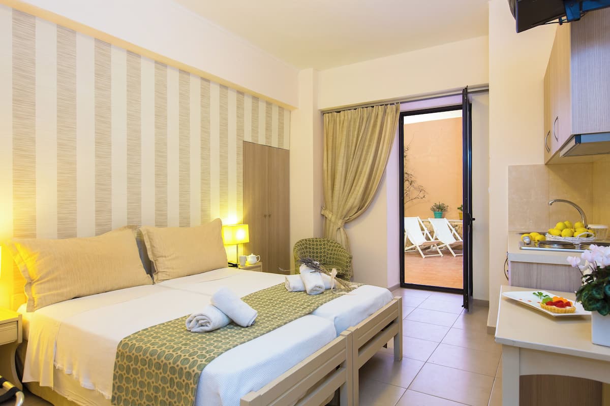 Quarto de hotel com cama, mesa de cabeceira, luminária e vista para a área externa com mesas e cadeiras.