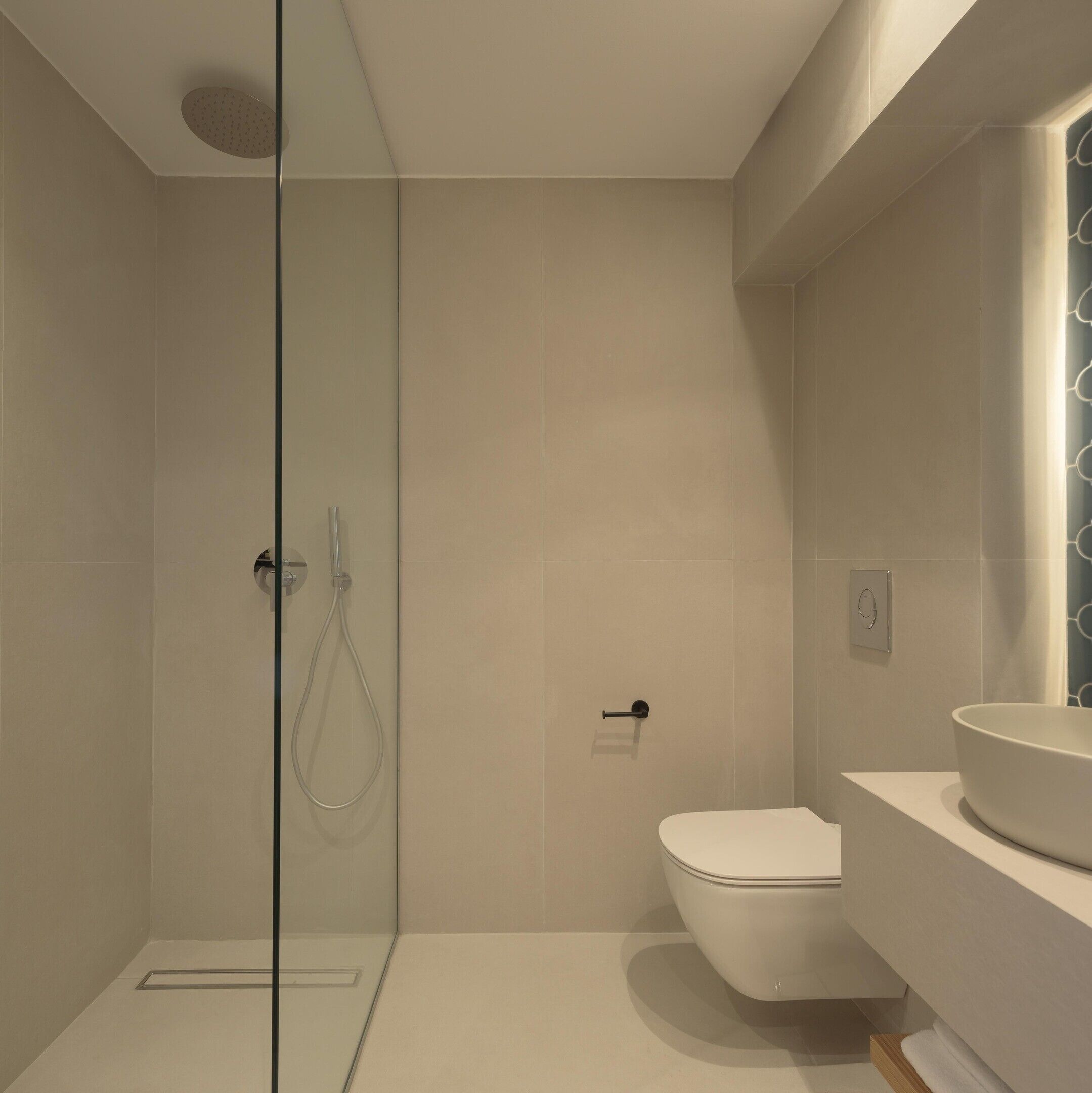 A modern bathroom with a glass shower enclosure, a white toilet, and a round sink.