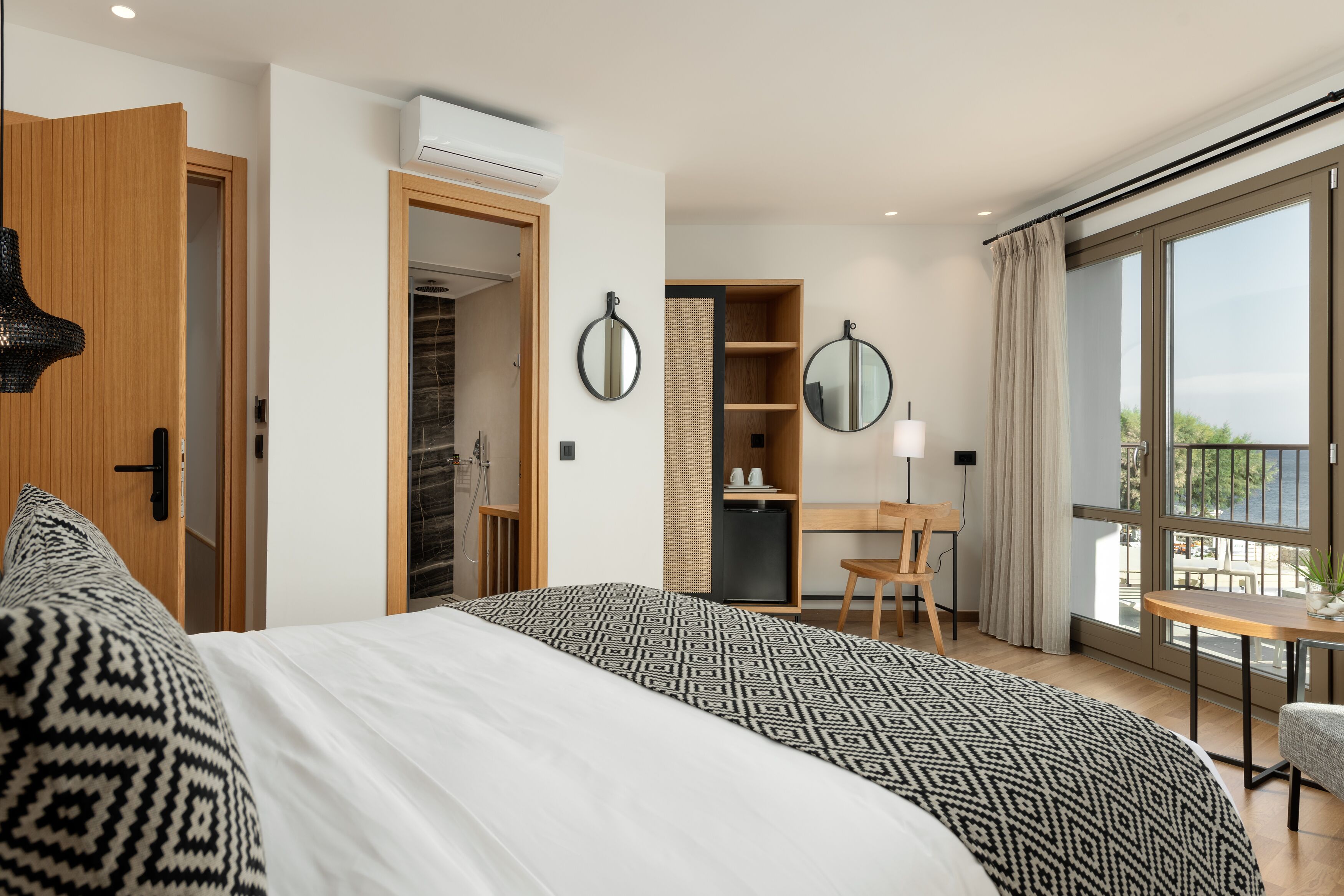 A modern hotel room with a large bed, a desk, and a balcony with a view.