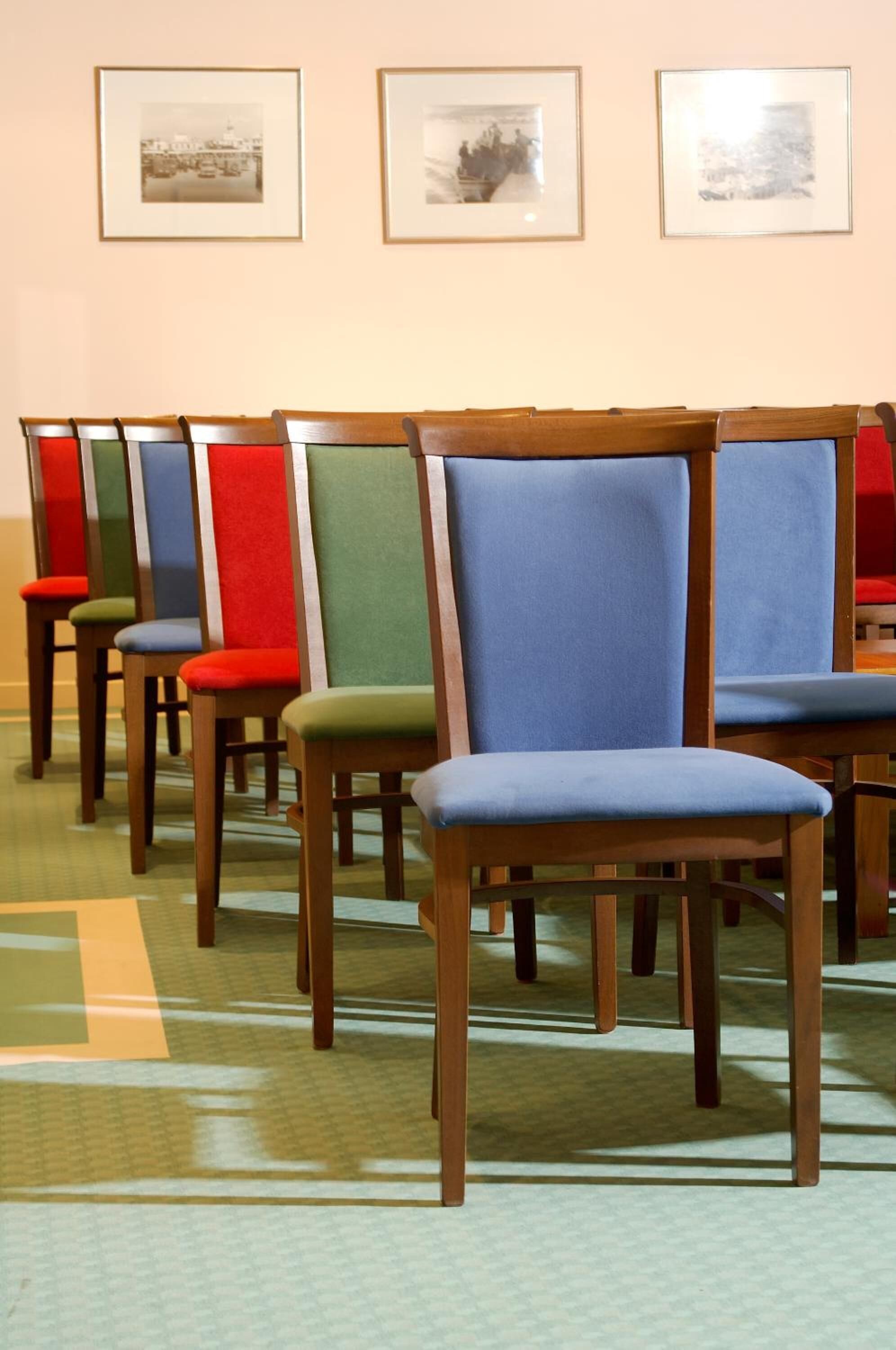 A row of wooden chairs with colorful upholstered seats and backs, arranged in a line on a patterned carpet.