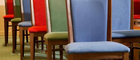 A row of wooden chairs with colorful upholstered seats and backs, arranged in a line on a patterned carpet.