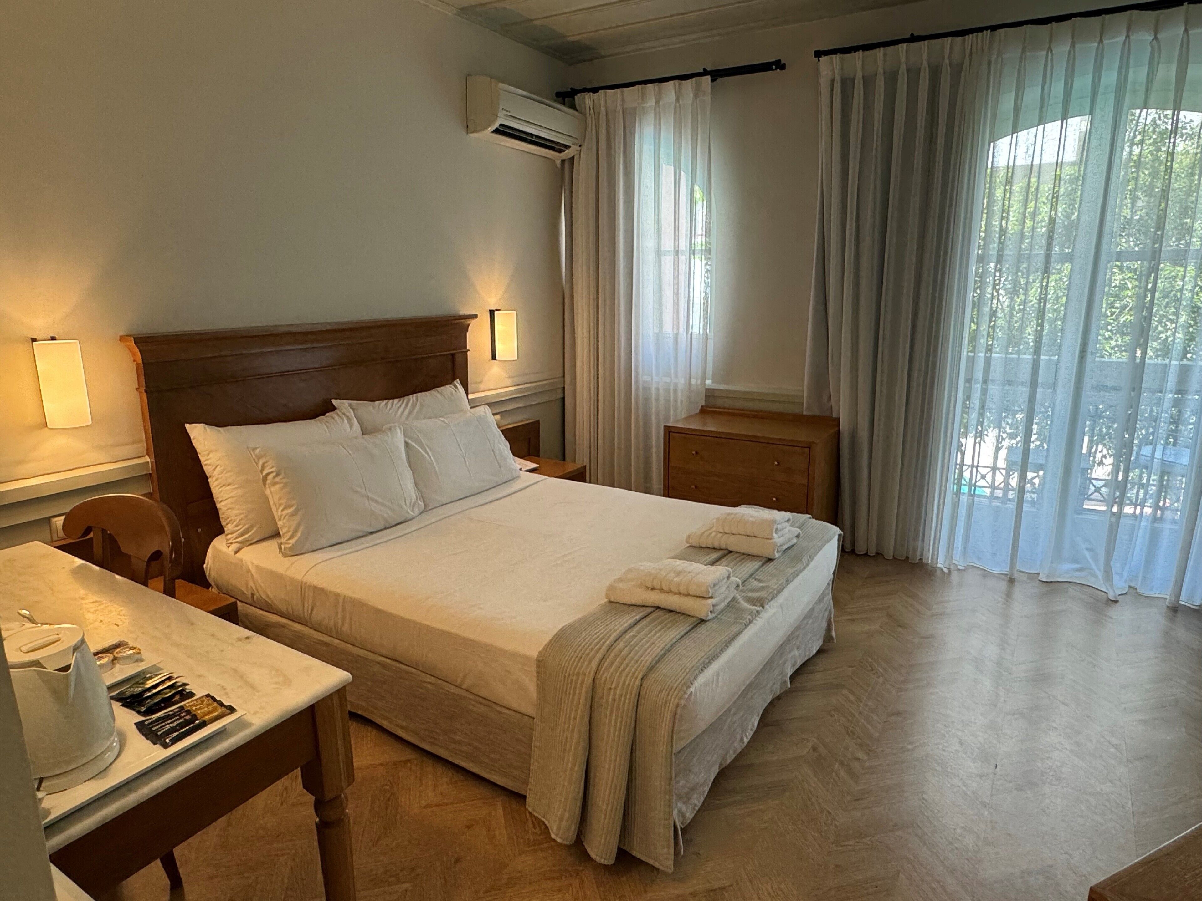 Habitación de hotel con cama, mesitas de noche, escritorio con tetera y cortinas.
