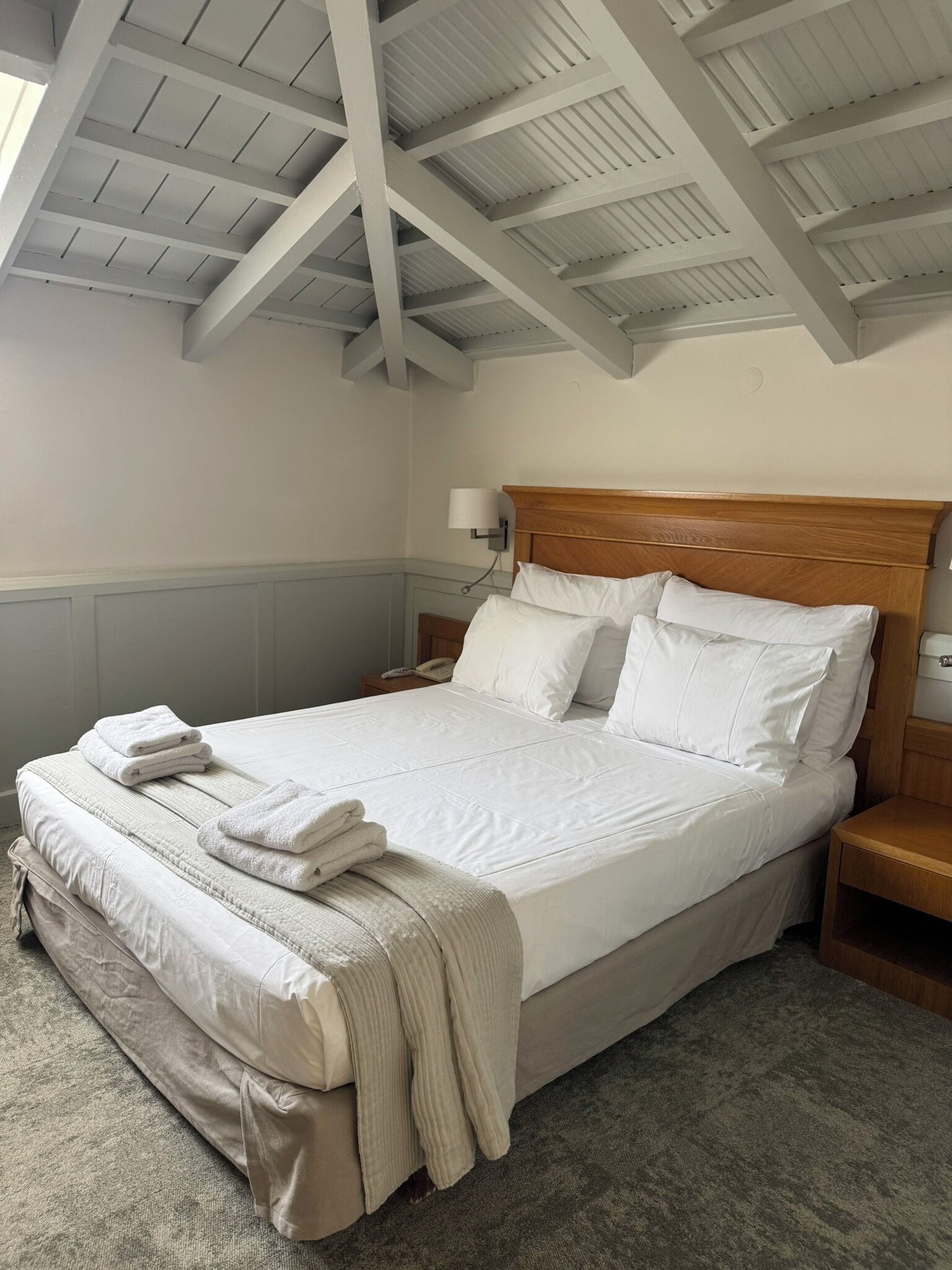 A neatly made bed in a room with a high ceiling and exposed beams.