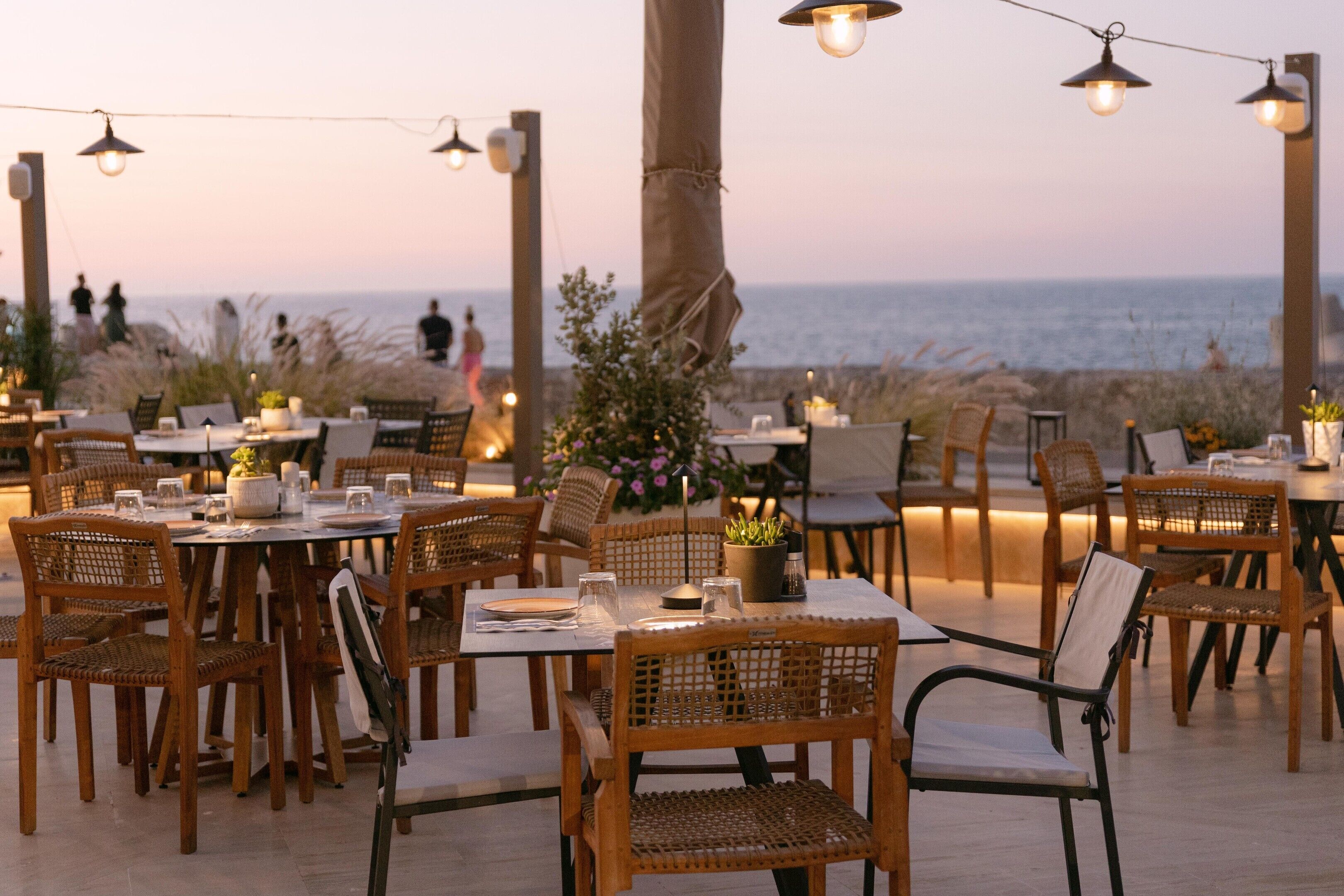 Un área de comedor al aire libre con mesas y sillas, con vista al mar.