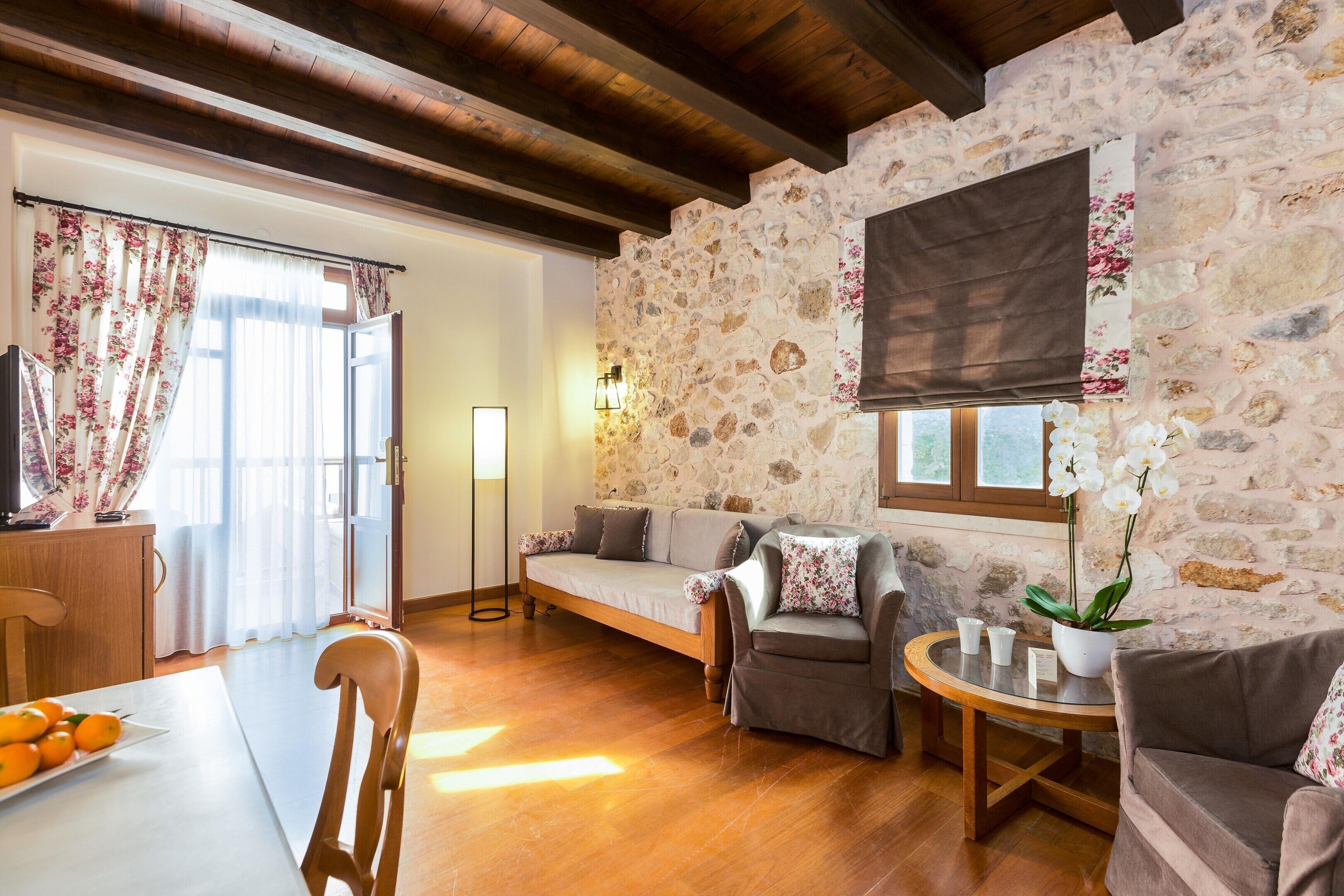 A cozy living room with a stone wall, wooden flooring, a sofa, a chair, a small table, and a potted plant.